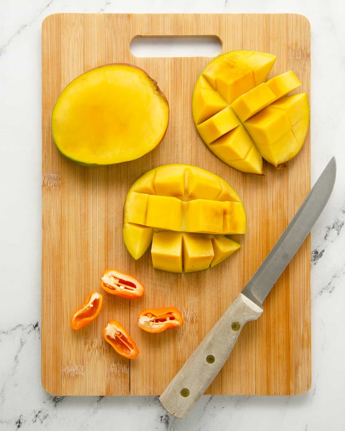 Two halves of a mango cubed with the middle seed to the side while two habaneros are sliced in half lengthwise.
