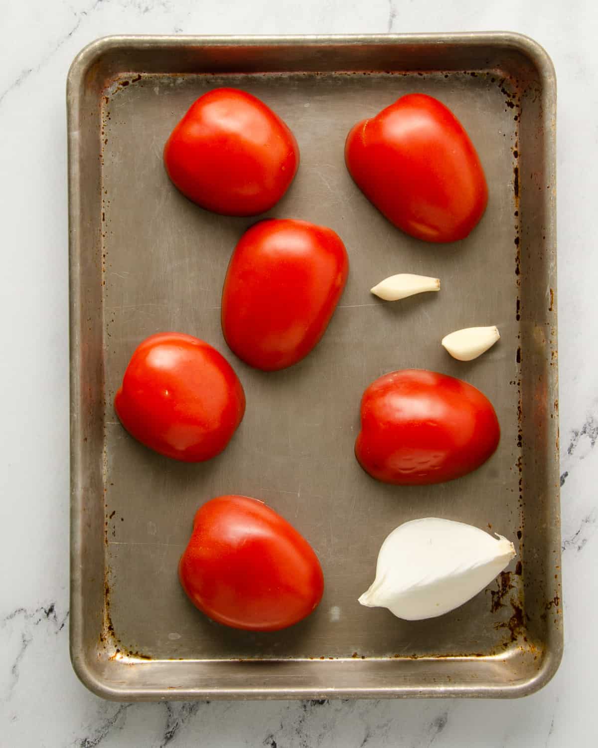 Roma tomato halves on a sheet tray with a quarter white onion and two garlic cloves.