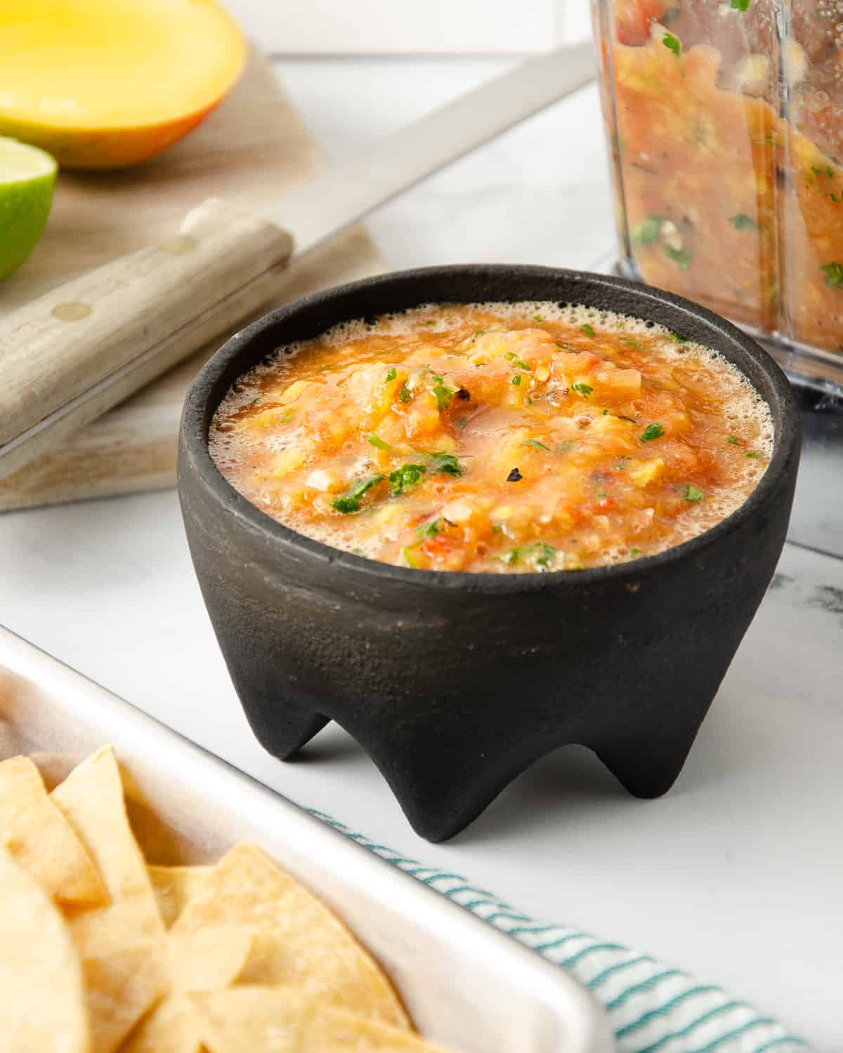 Salsa in a molcajete with the blender filled with more salsa to the right and homemade tortilla chips to the left.