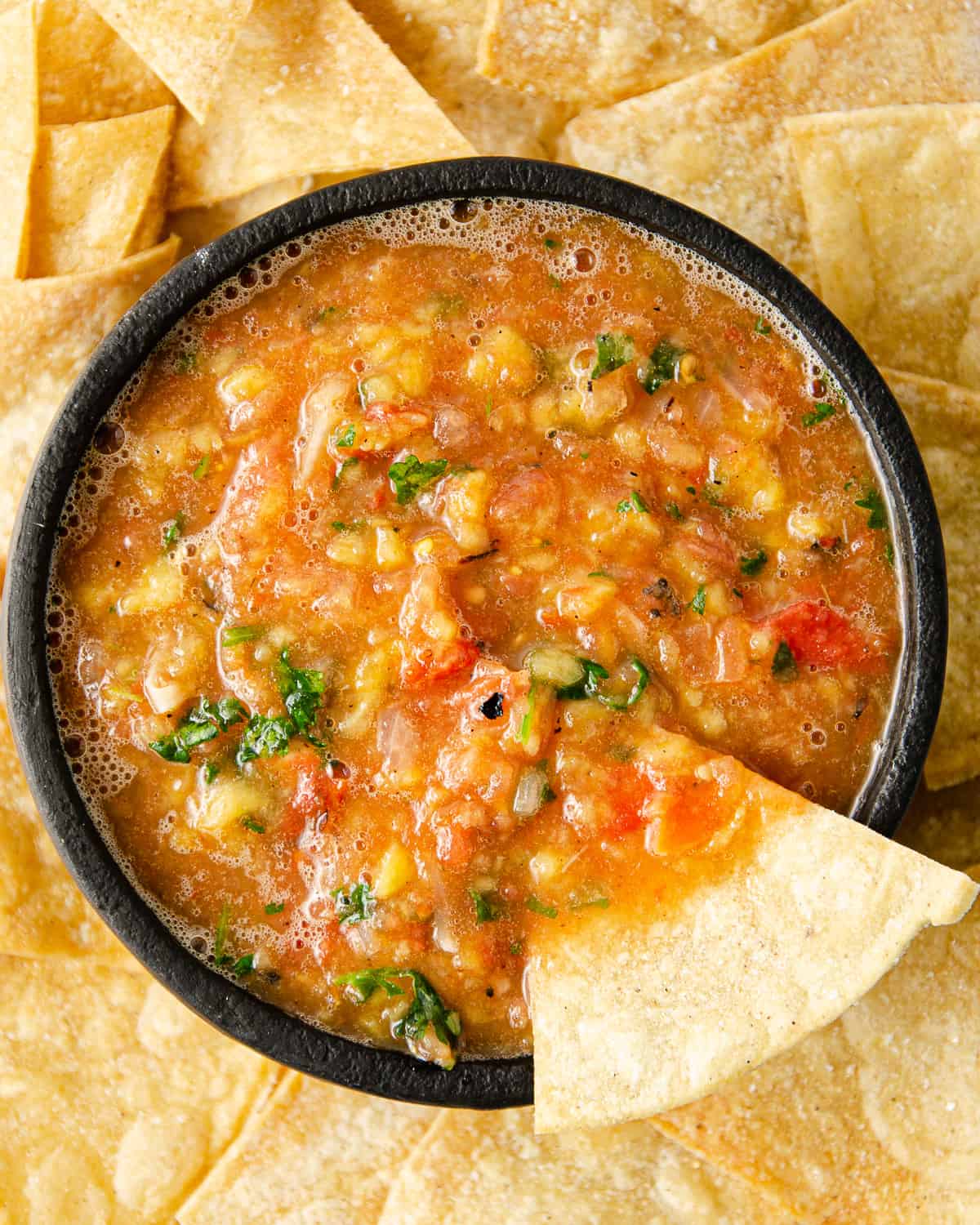 A brightly colored red and orange mango habanero salsa in a molcajete surrounded by tortilla chips.