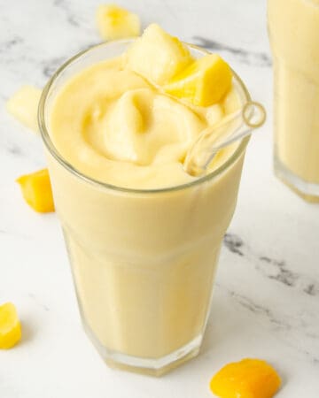 A glass of pineapple and mango smoothie swirled in a glass with a straw.
