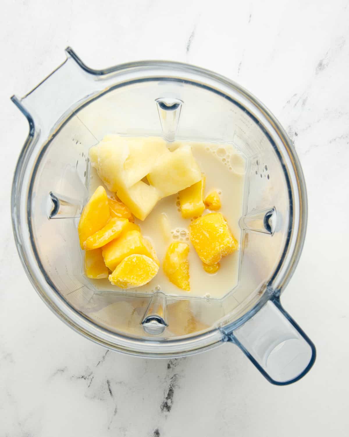 Frozen pineapple and mango in a blender with coconut milk.