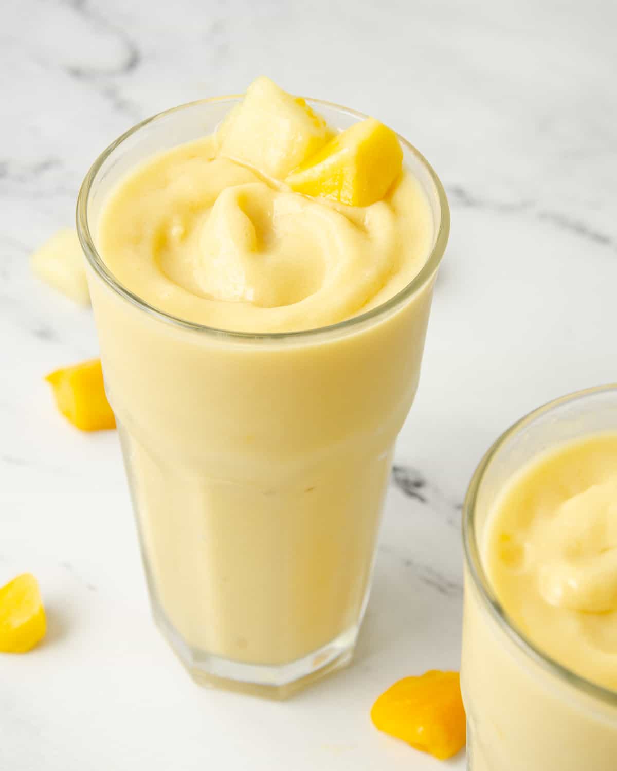 Tall glass filled with a yellow pineapple mango smoothie inside.