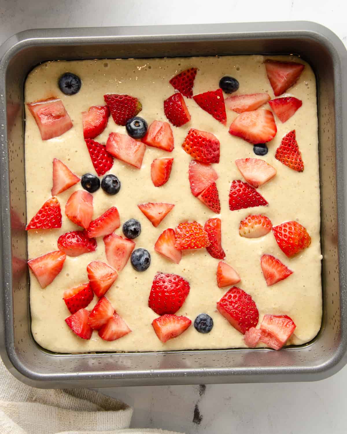 Baked oats batter in a baking dish with strawberries and blueberries on top before baking.