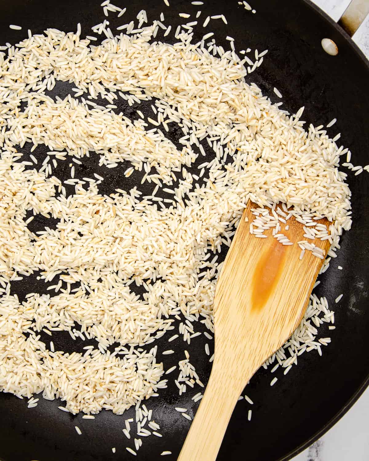 Toasted rice in a large skillet with a wooden spoon stirring.