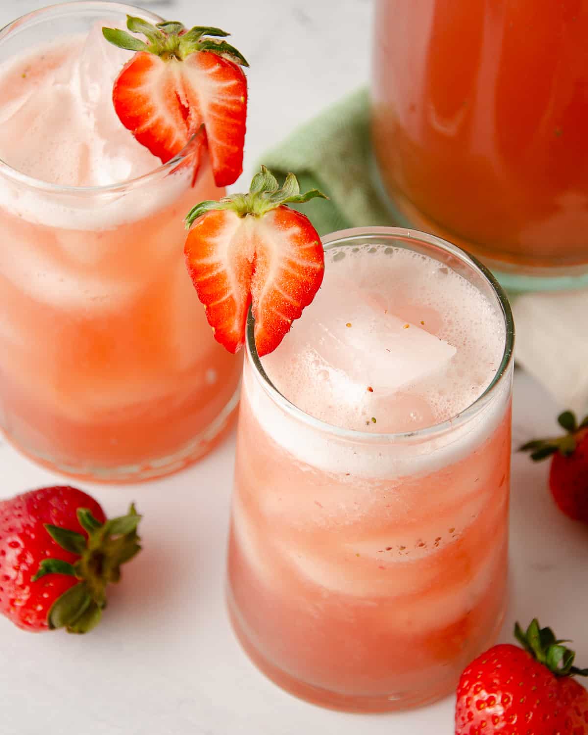 Two glasses of agua de fresa topped with strawberry slices.