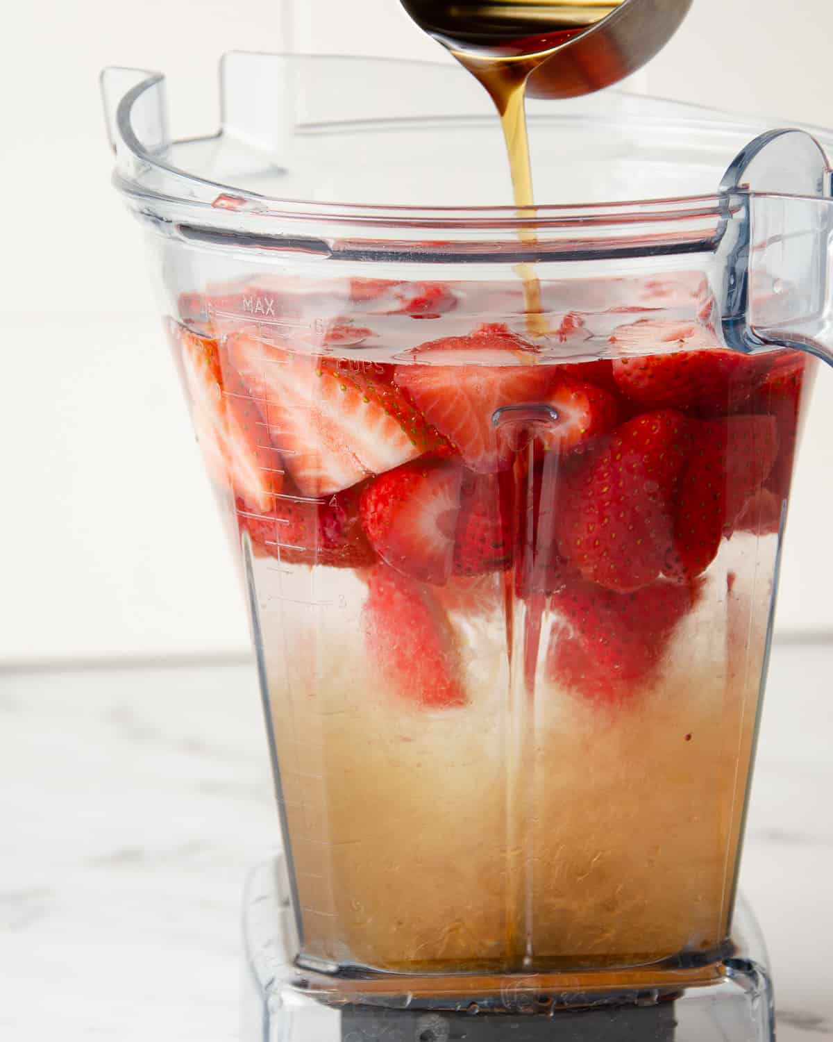 A blender with water, whole strawberries, and sweetener.