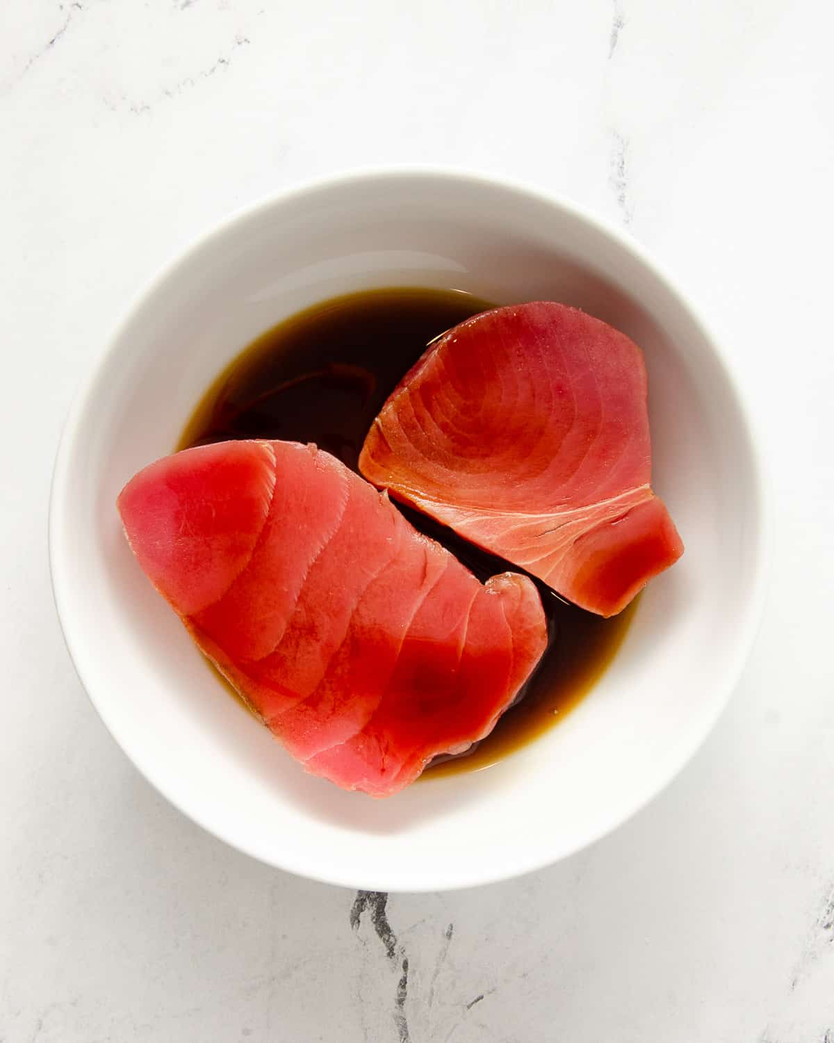 Two pieces of raw ahi tuna in a white bowl with coconut aminos.