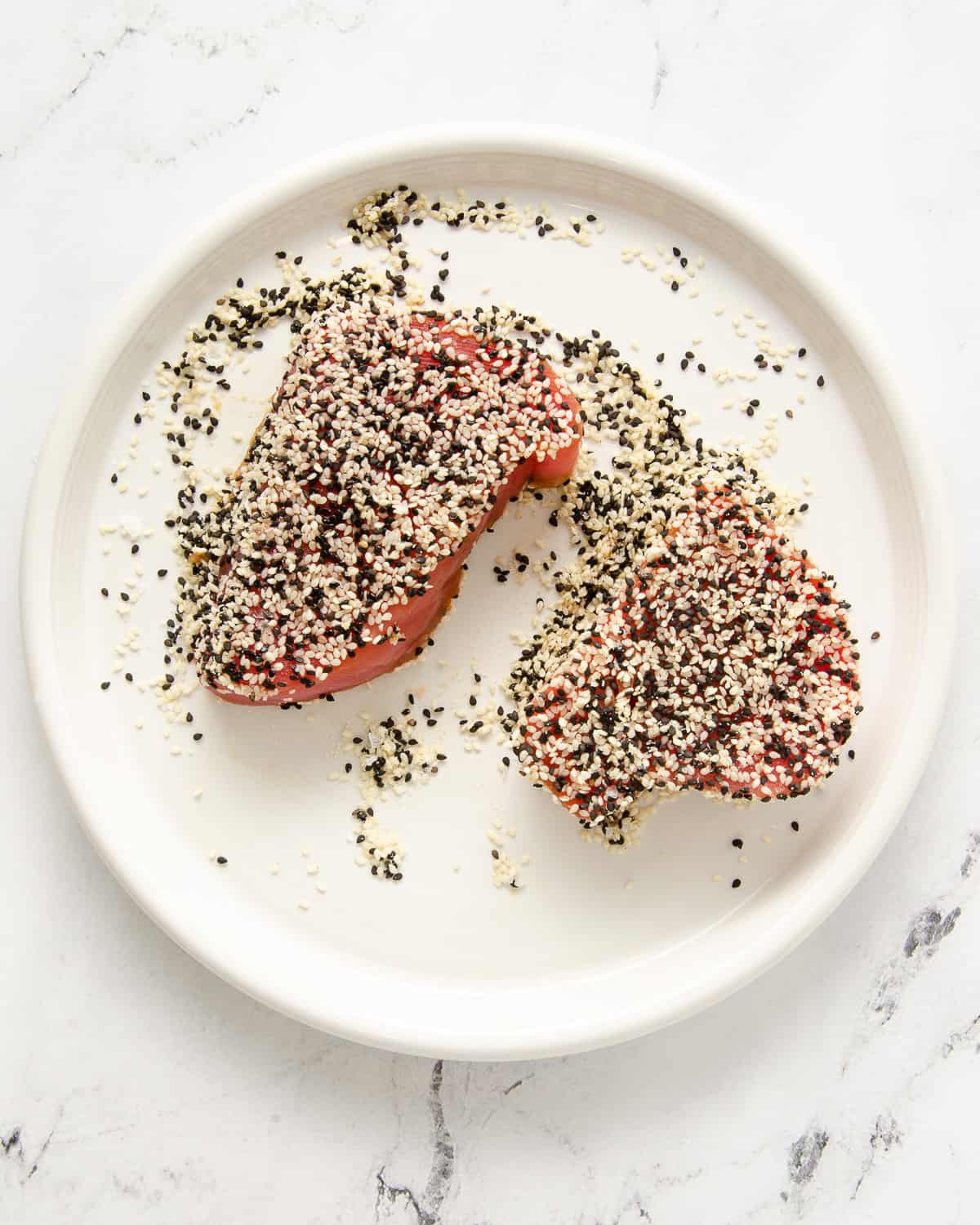 Raw ahi tuna topped with black and white sesame seeds on a white plate.