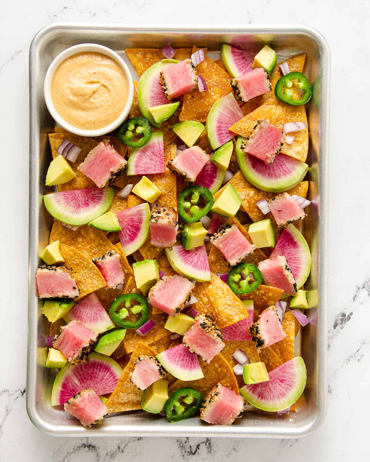 Baking tray with tortilla chips topped with radishes, red onions, avocado, and jalapeños.