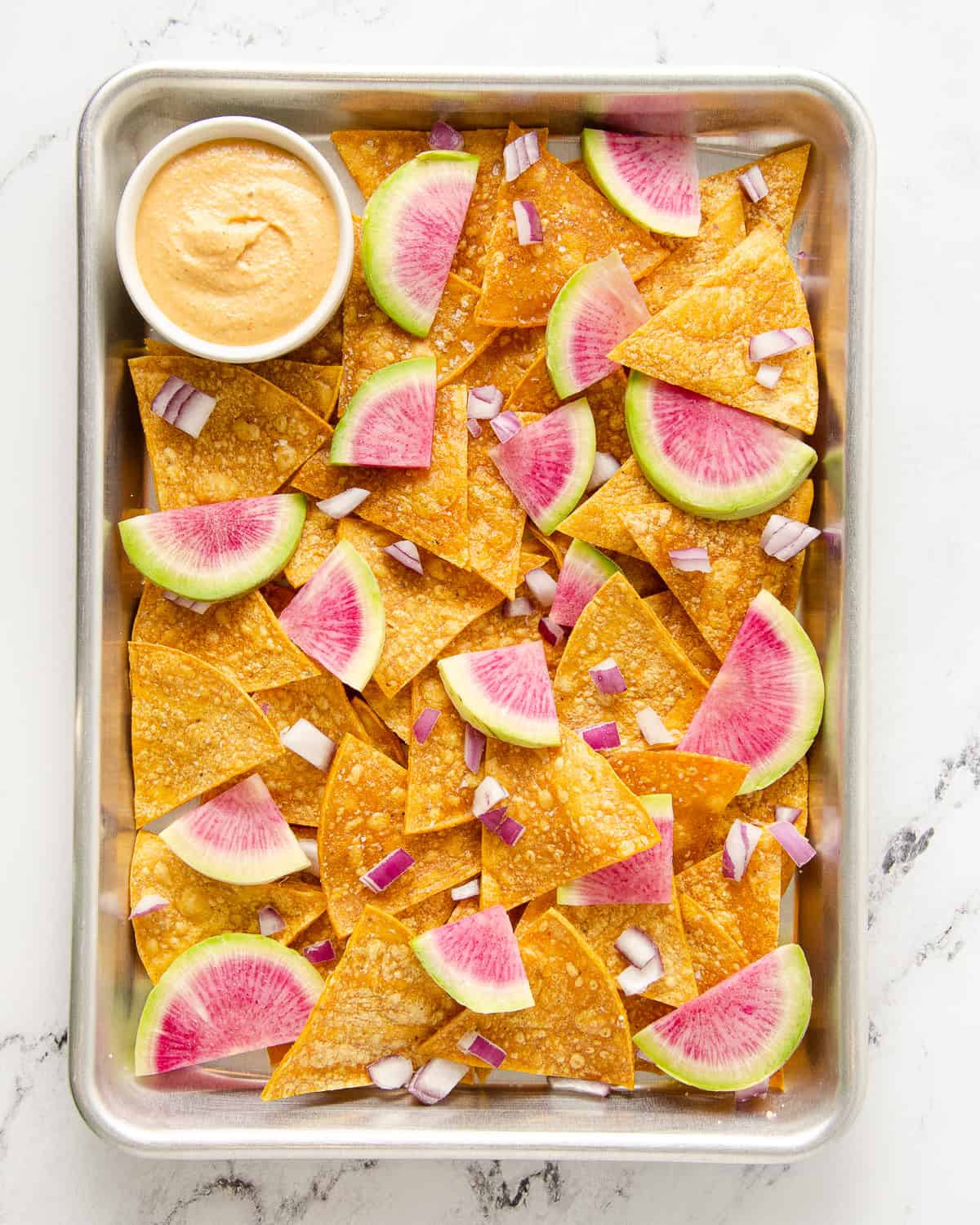 Baking tray with tortilla chips topped with radishes and red onions.