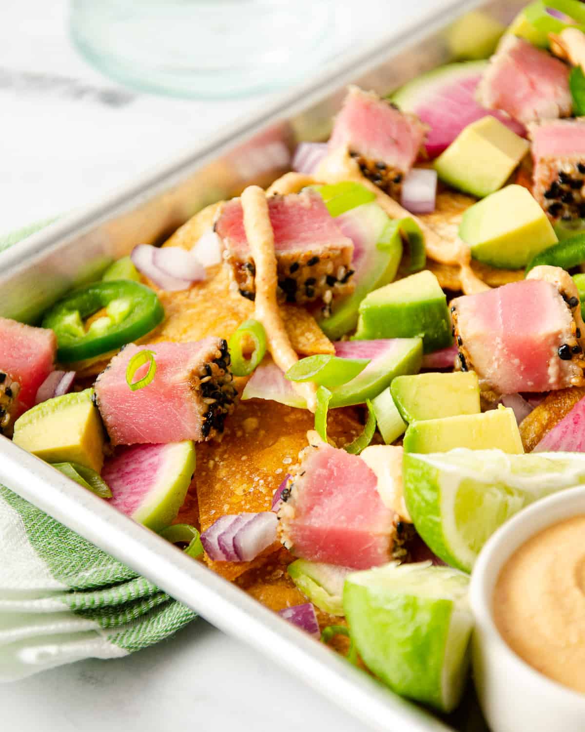 A baking tray full of ahi tuna nachos topped with jalapeños, radishes, green onions, and sriracha mayo.