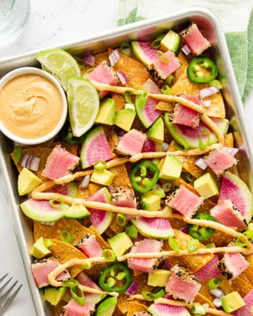 A baking tray full of ahi tuna nachos with jalapeños, radishes, green onions, and sriracha mayo.