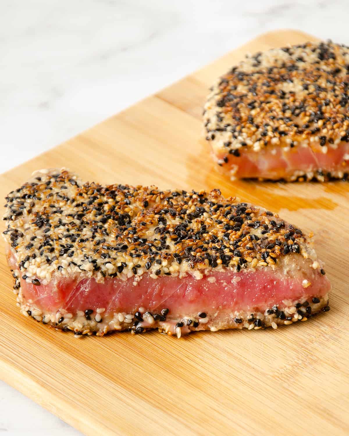 Two pieces of sesame crusted seared ahi tuna on a cutting board.