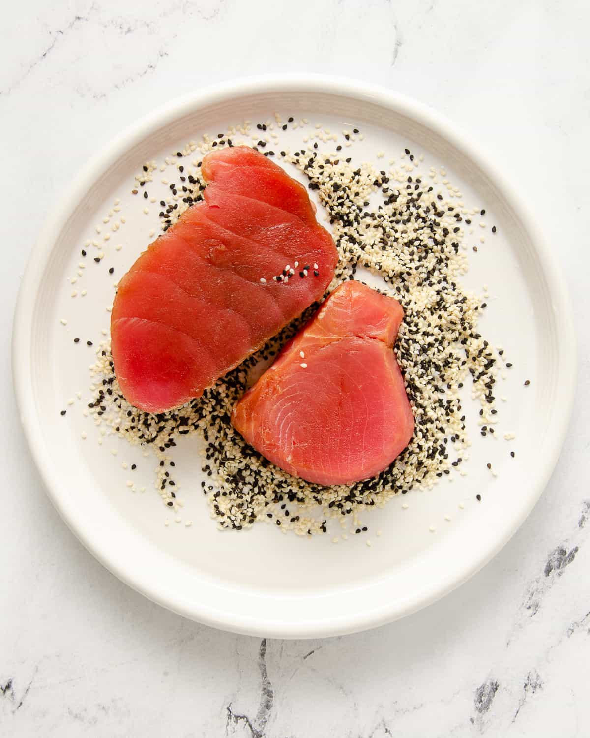 Raw ahi tuna in a white plate full of black and white sesame seeds.
