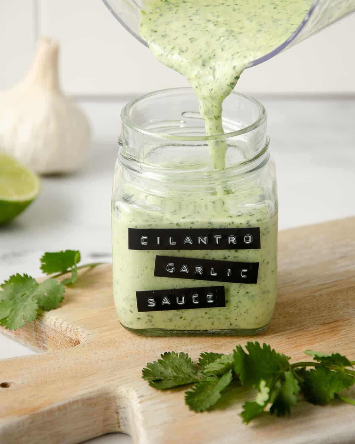 Pouring cilantro garlic sauce into a labeled jar on a cutting board.