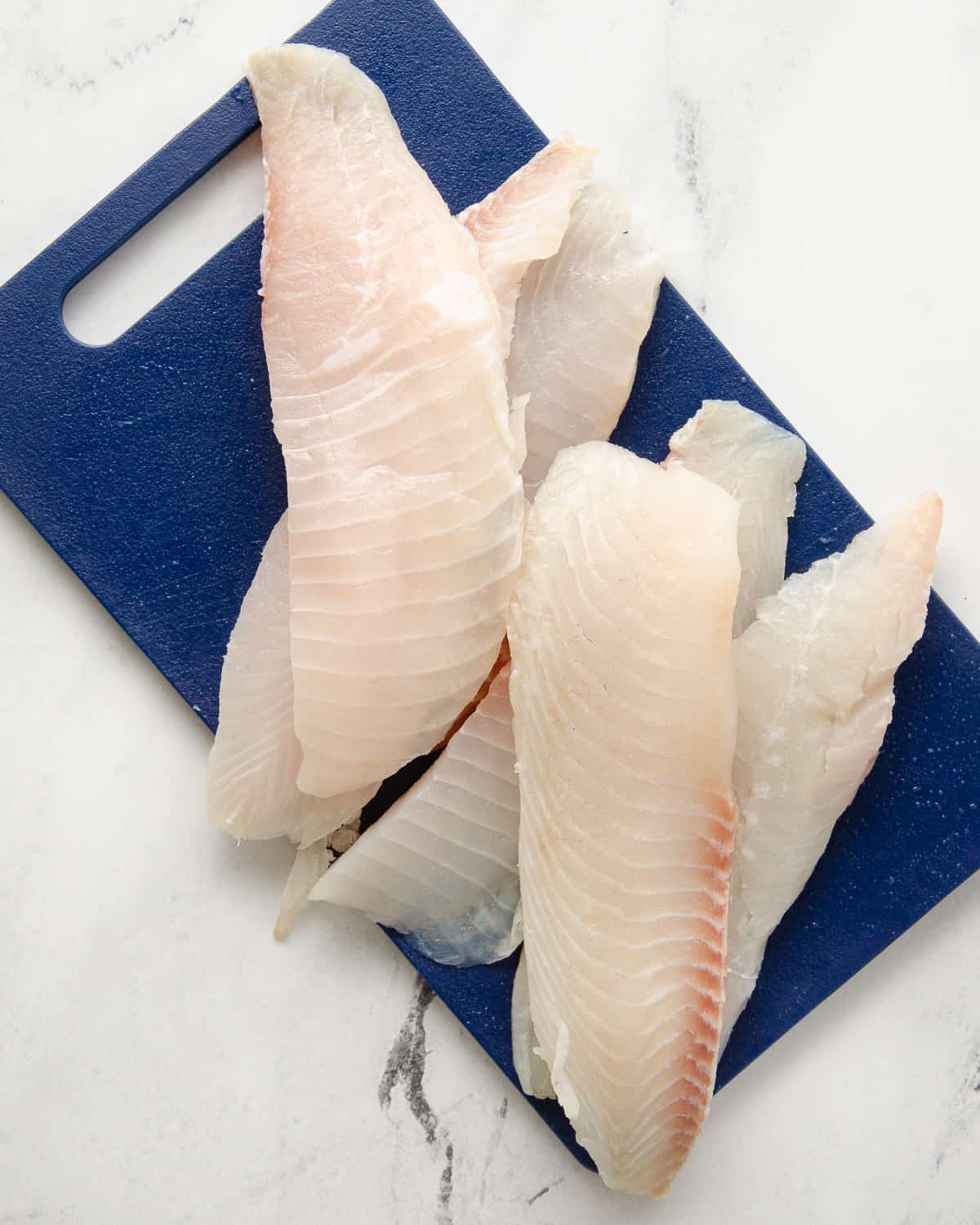 A blue cutting board with tilapia filets.
