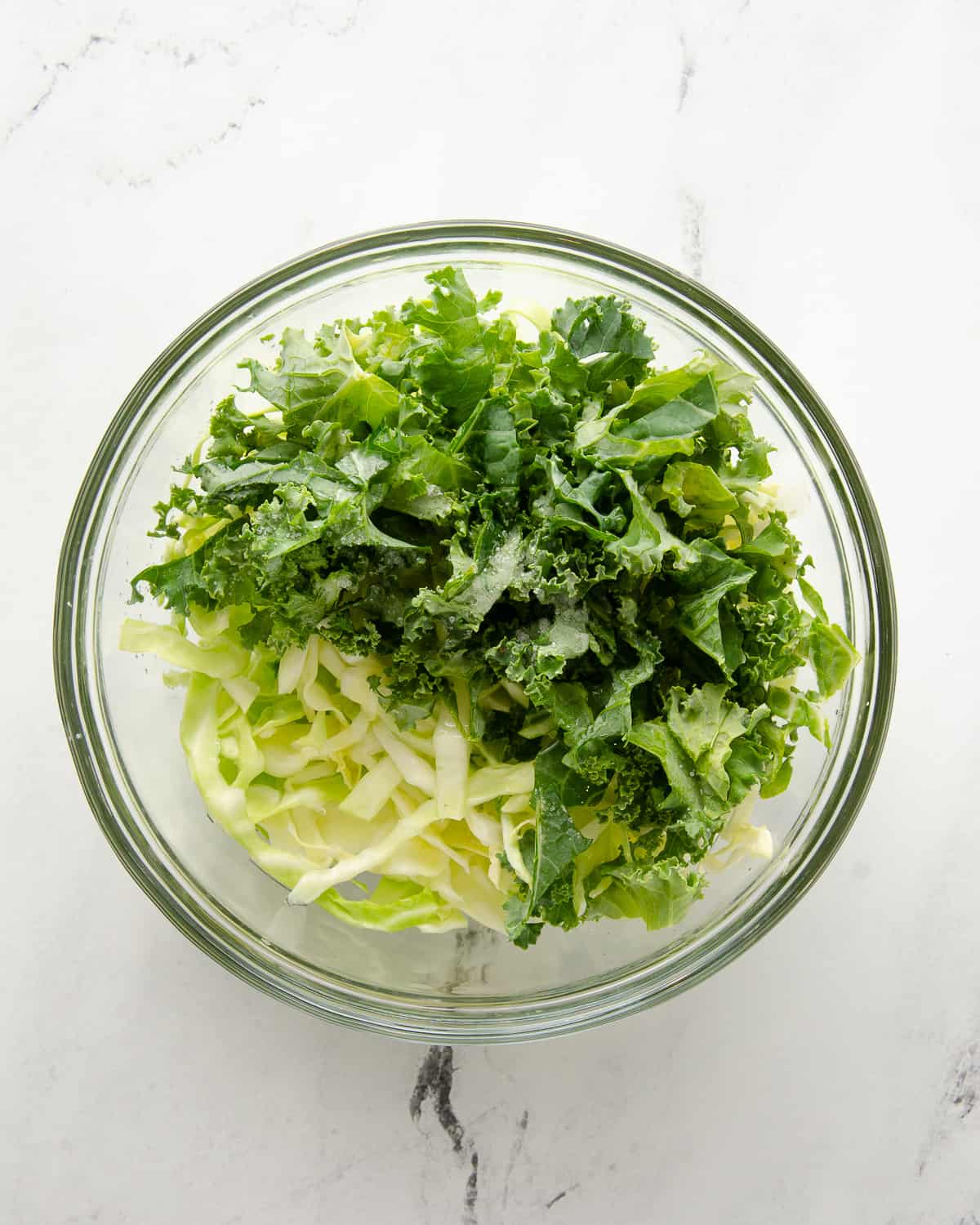 A glass bowl full of shredded cabbage and kale.