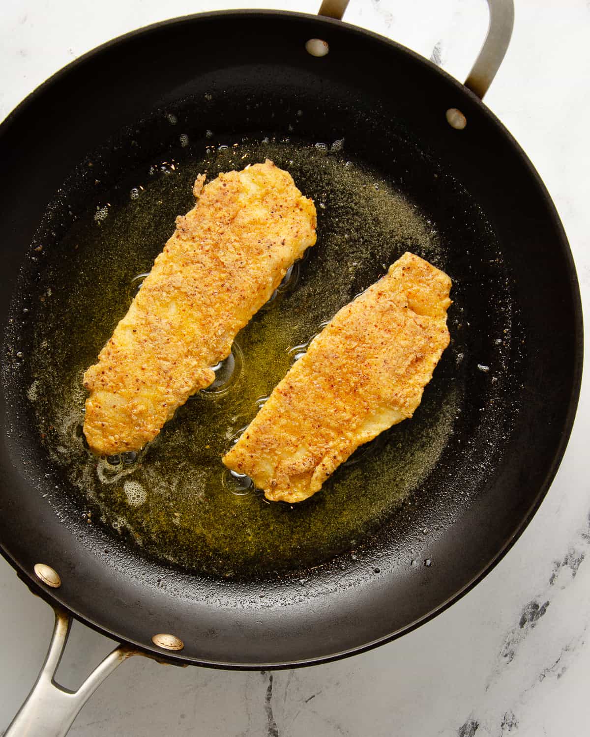 Two pieces of fried tilapia in a frying pan.
