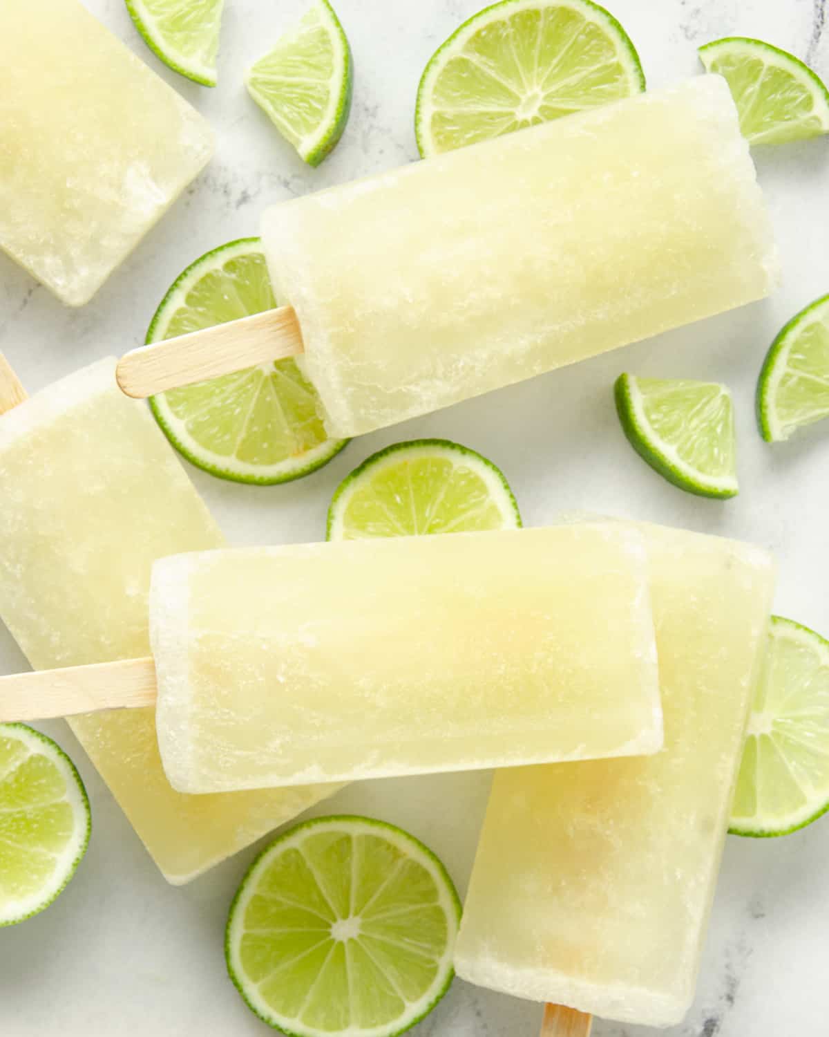 A layer of lime popsicles and lime wedges on marble.