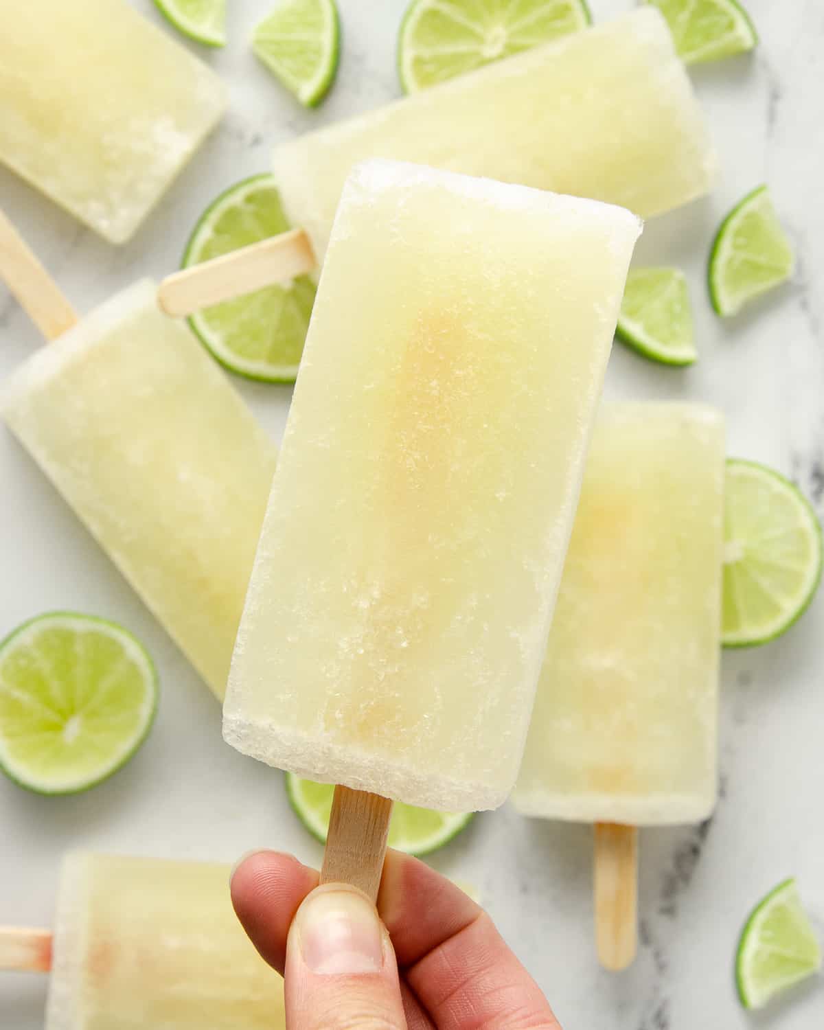 A hand holding a lime popsicle over a few other popsicles on the table.