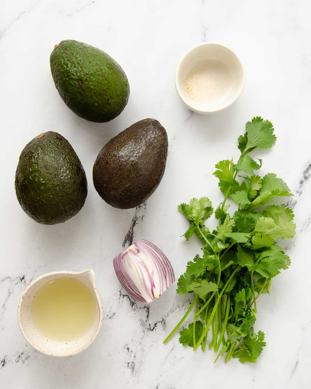 Ingredients to make a Mexican avocado salad laid on a marble counter.