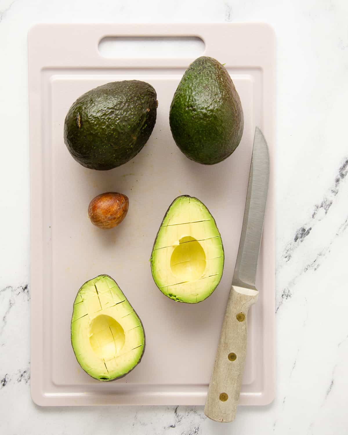 Two avocado halves on a cutting board with the pit removed and the flesh cut both vertically and horizontally to make it easier to remove from the skin.