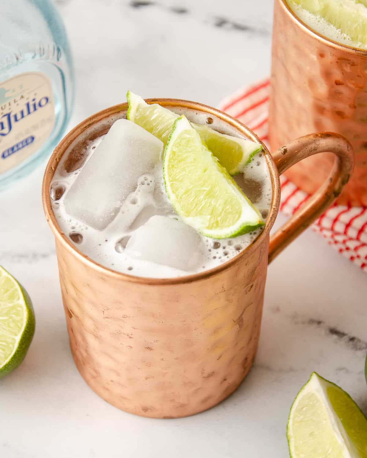 Close up view of a tequila mule in a copper mug with two lime wedges inside.