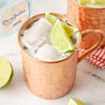 A featured image of a tequila mule in a copper mug with two lime wedges inside.