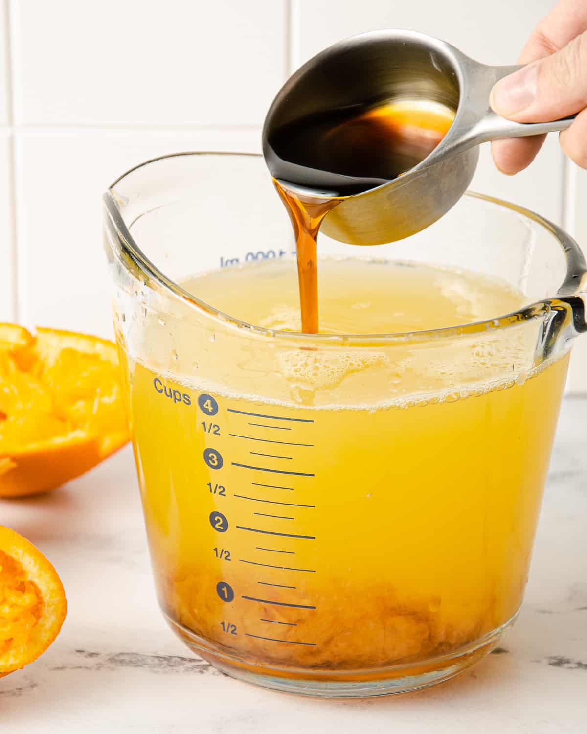 Pouring honey into a measuring cup of orange juice and water.