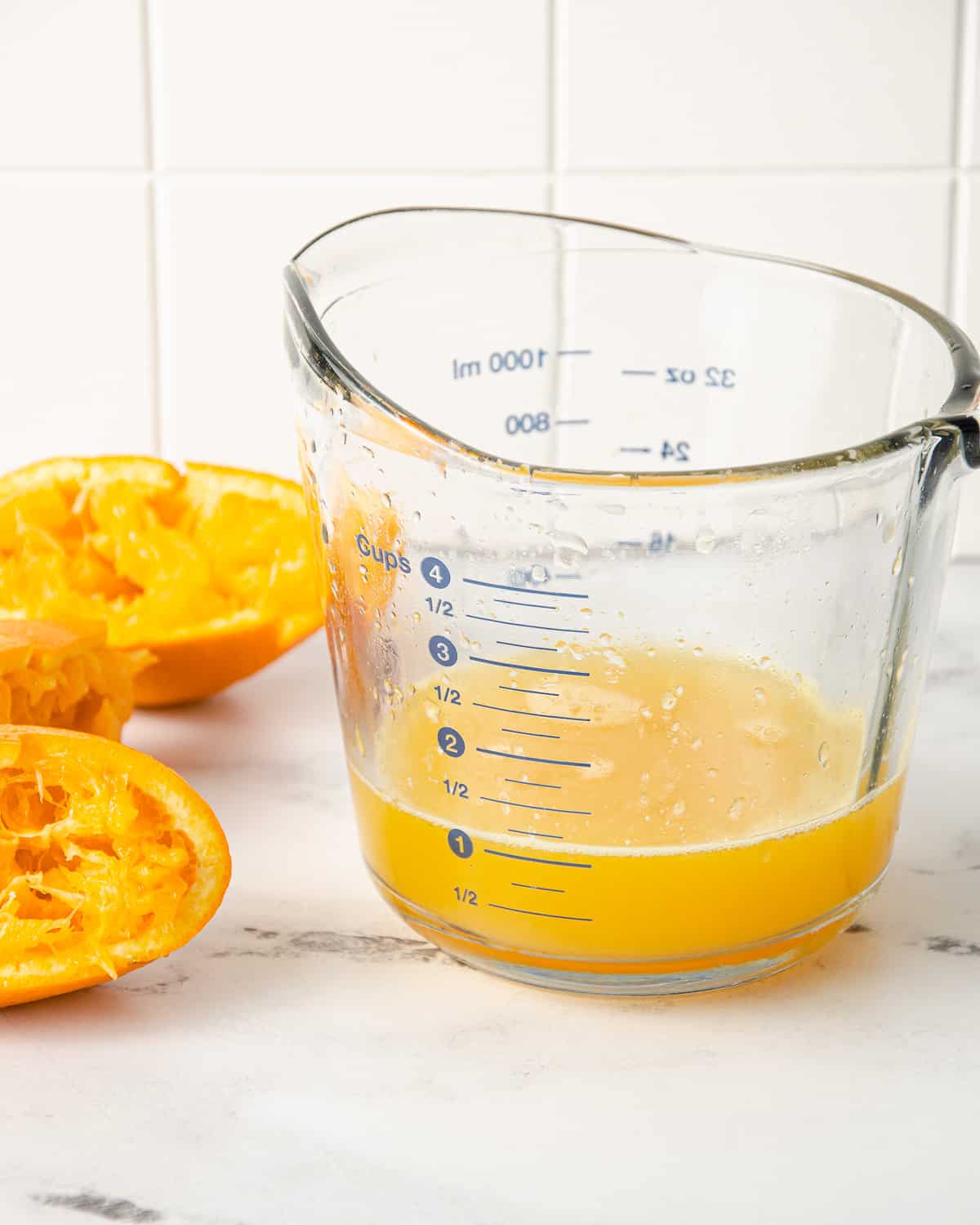 A measuring cup of freshly squeezed orange juice with squeezed orange peels to the side.
