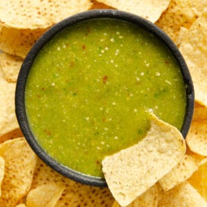 A bright green serrano salsa verde in a molcajete with a chip being dipped into it.