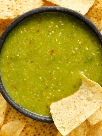A bright green serrano salsa verde in a molcajete with a chip being dipped into it.