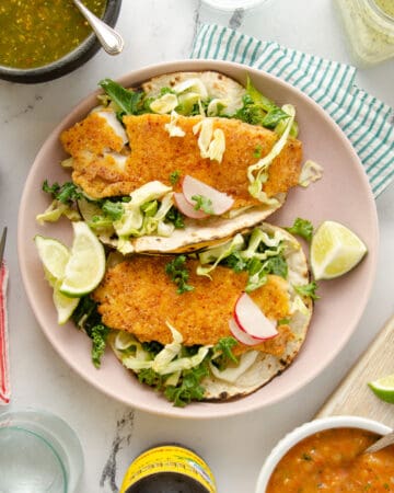 A featured image of a plate of two fish tacos surrounded by sides to pair with it.