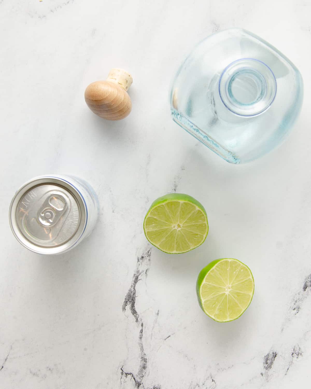 Ingredients to make a Mexican mule on marble: a lime, tequila bottle and can of ginger beer.