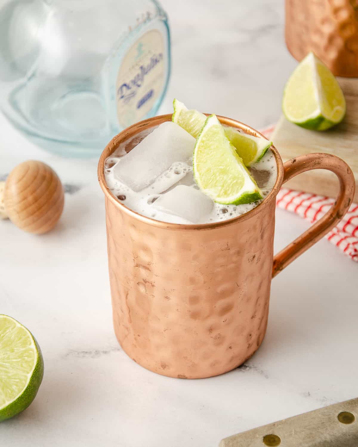 A copper mug with a tequila mule inside it on a marble counter with a bottle of tequila behind it.
