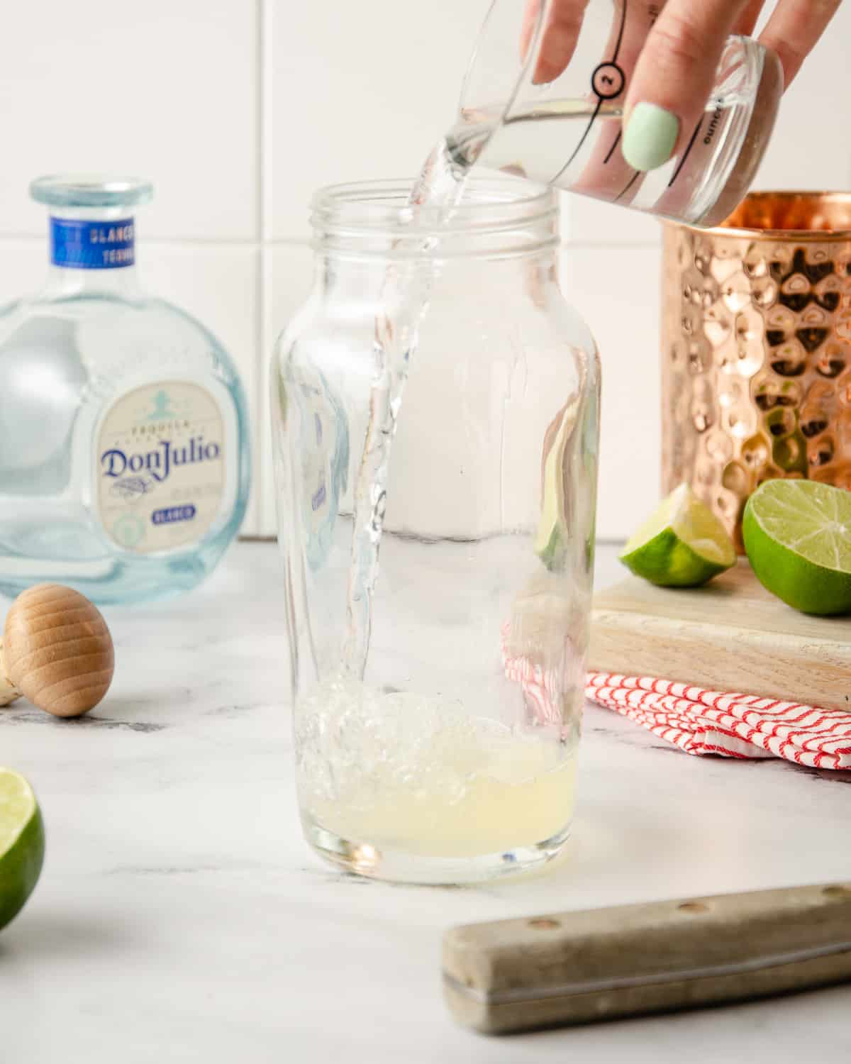 Pouring tequila into a cocktail shaker of lime juice.