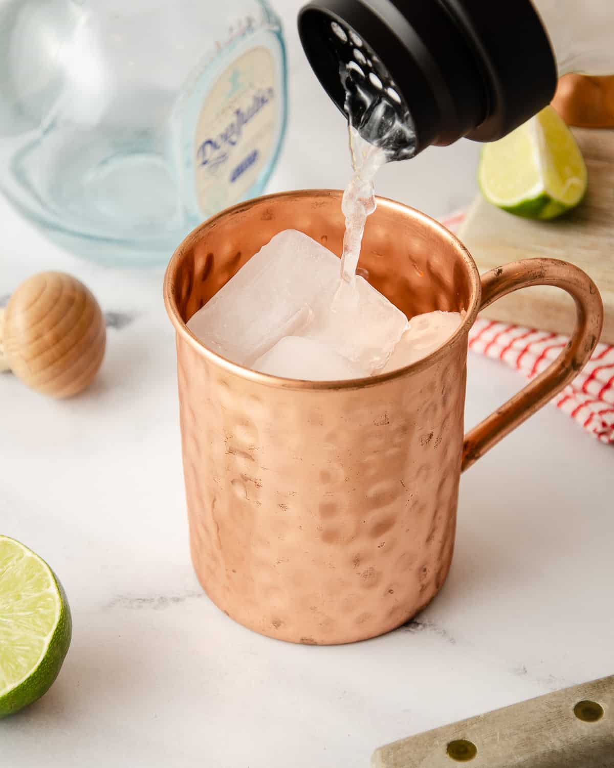 Straining tequila mule liquid into a copper mug filled with ice.