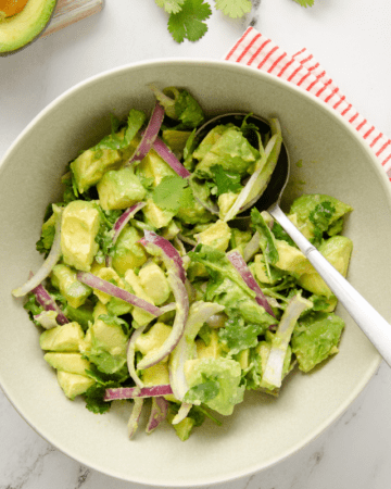 A large bowl with an avocado salad with a large silver spoon inside.