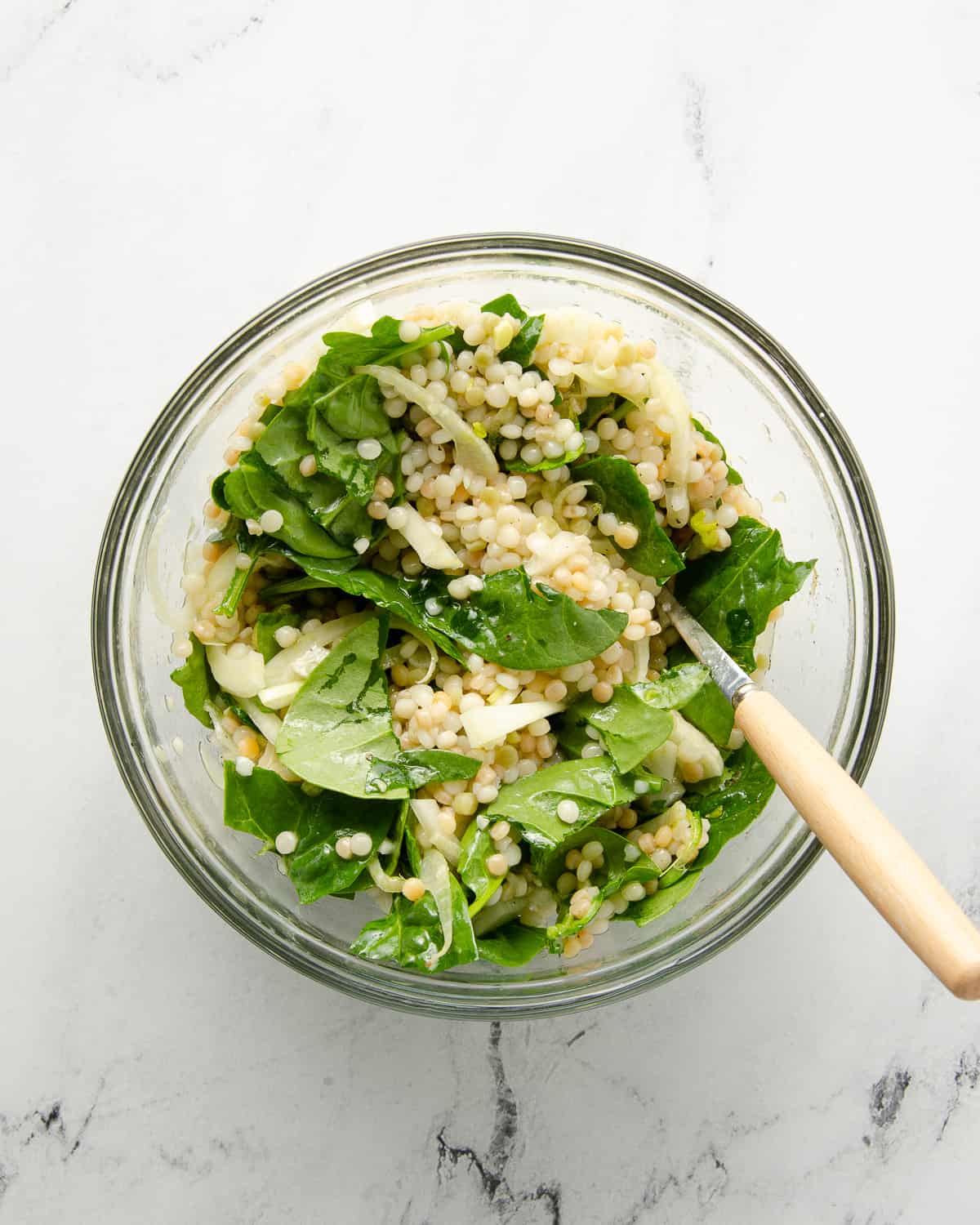 A glass bowl of fresh couscous salad with spinach and fennel.