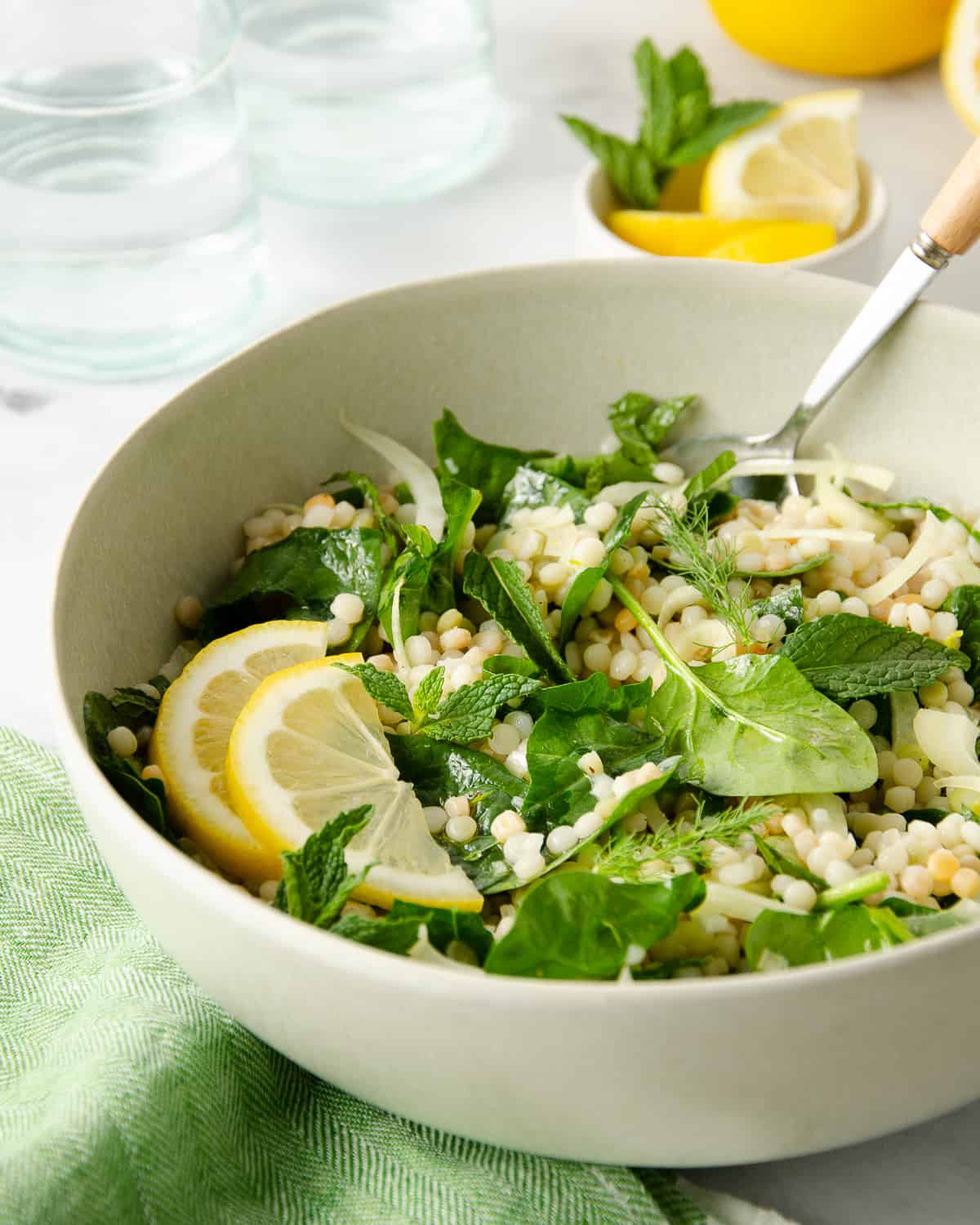 A bowl full of couscous salad topped with spinach, fresh mint, and lemon slices.