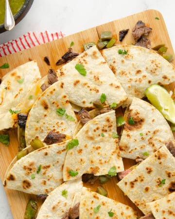 A featured image of layers of quartered carne asada quesadillas on a cutting board.
