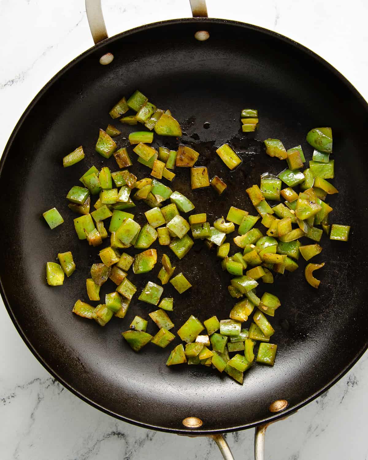 Small diced green bell pepper cooked in a skillet.