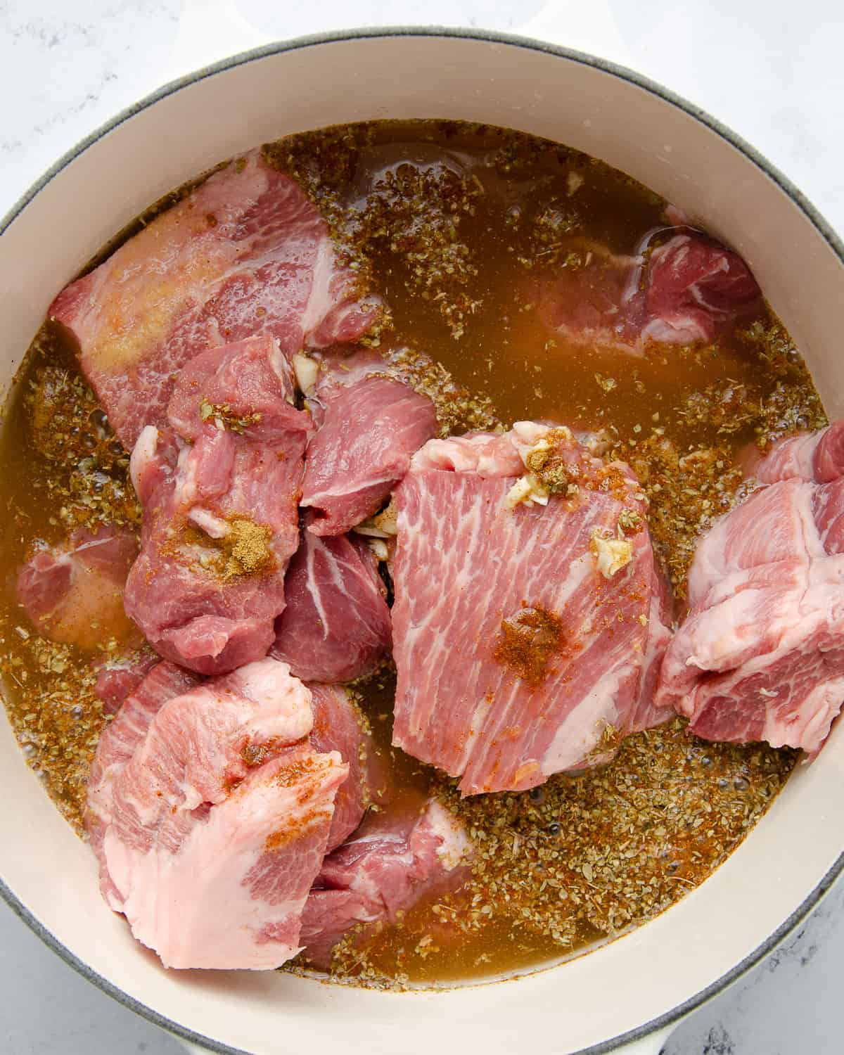 Large chunks of boneless pork shoulder in a dutch oven filled with spices and broth.
