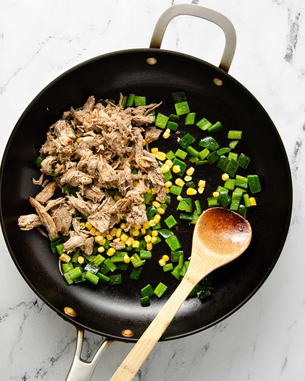 Adding carnitas and frozen corn to cooked poblano in a skillet.