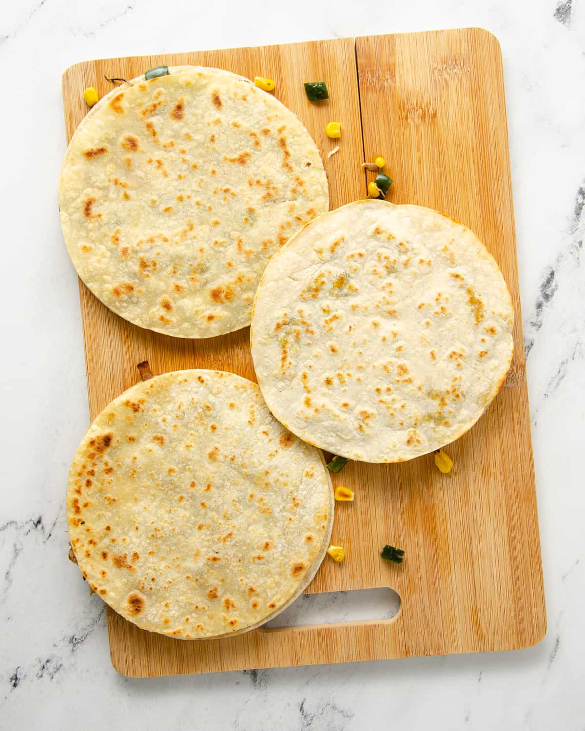 Three quesadillas cooked through on a cutting board ready to cut into pieces.