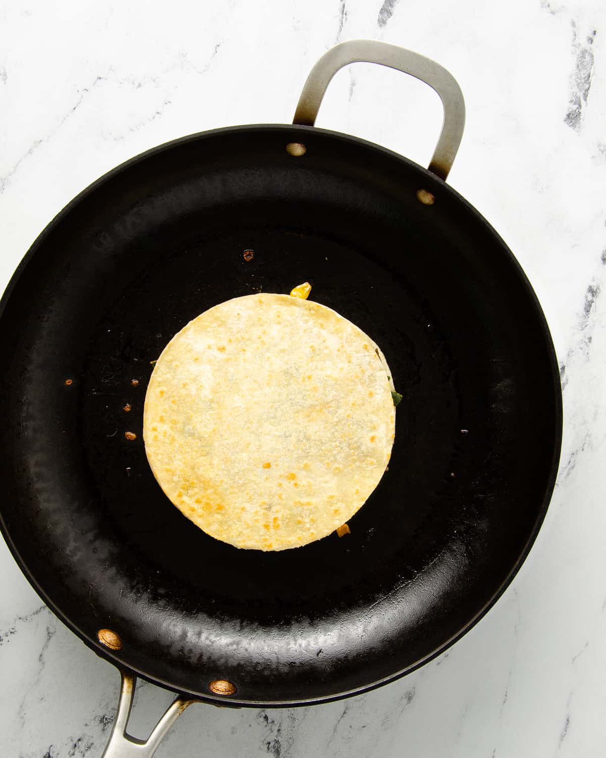 A cooked quesadilla flipped over in a skillet.