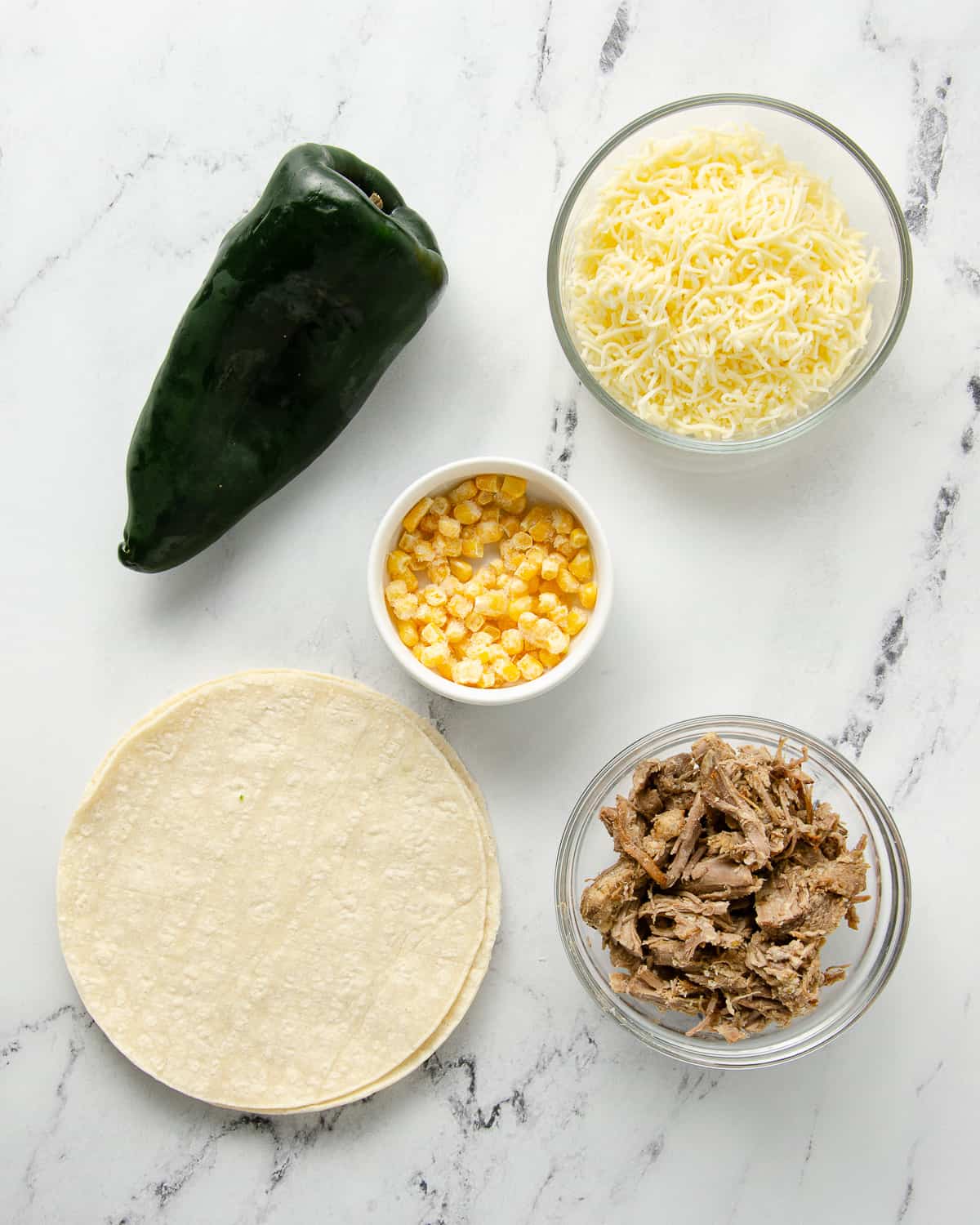 The ingredients to make a carnitas quesadilla sitting on a marble counter.
