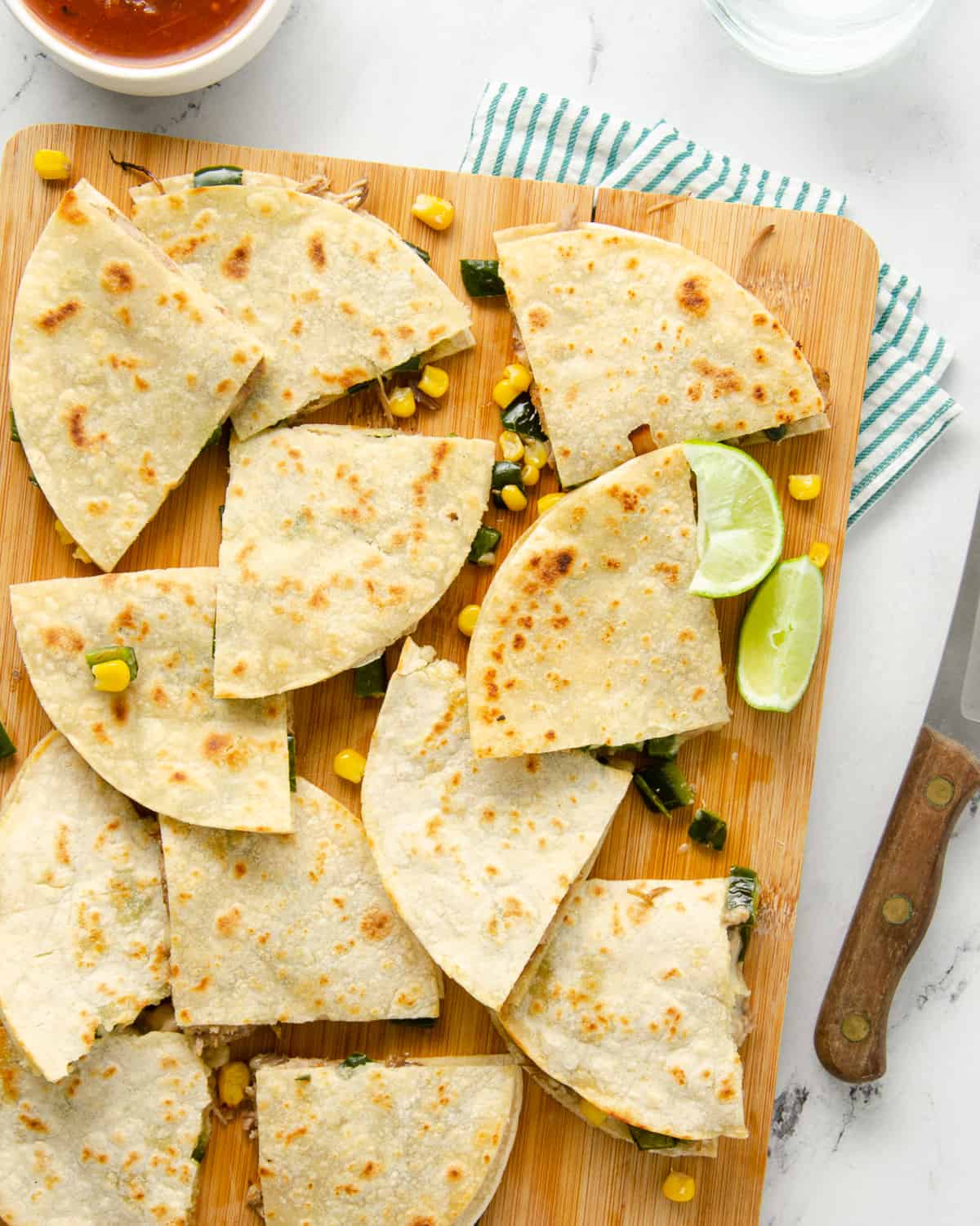 A cutting board topped with carnitas quesadillas cut into quarters.