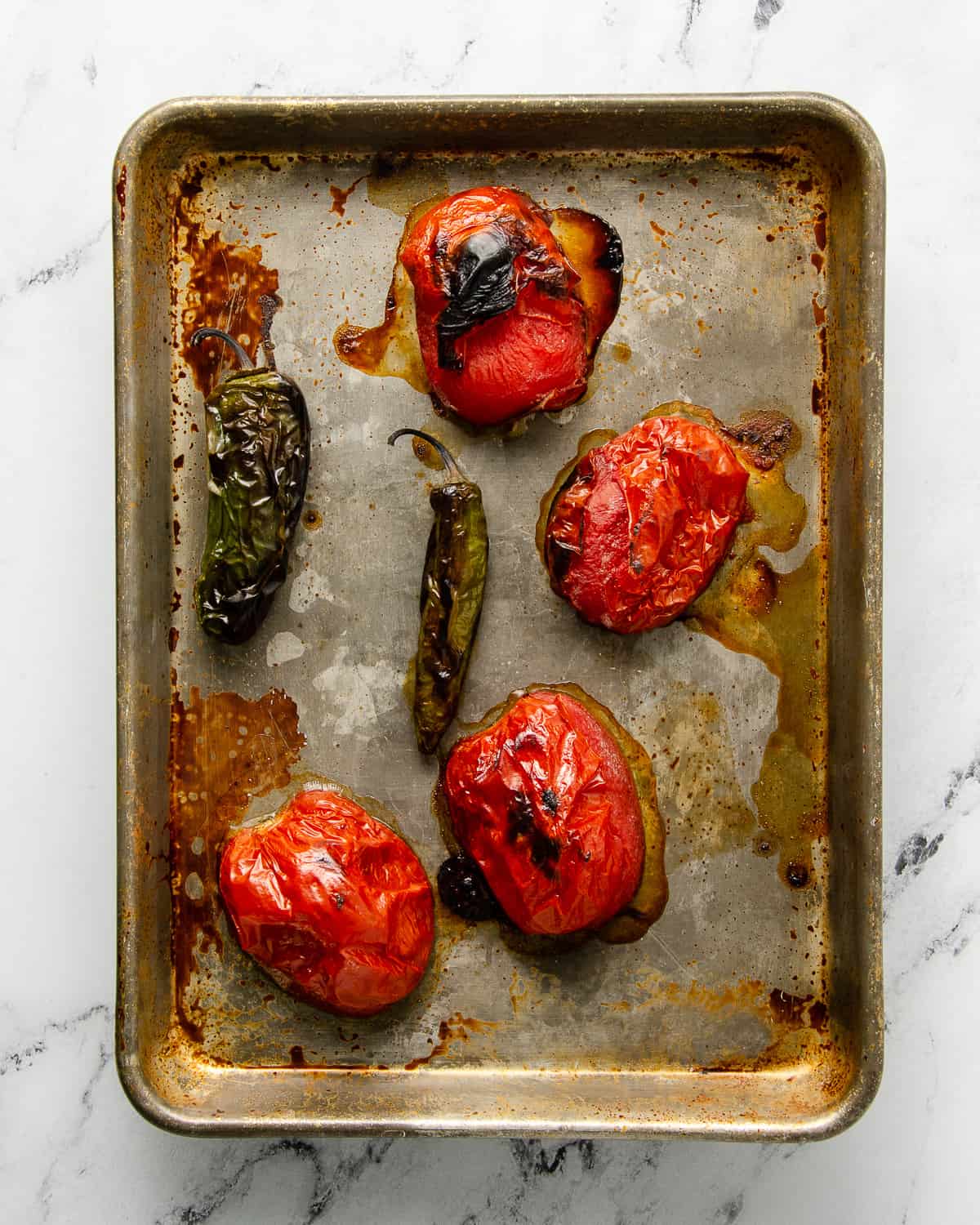 Broiled roma tomates, jalapeno and a serrano on an aluminum baking tray.